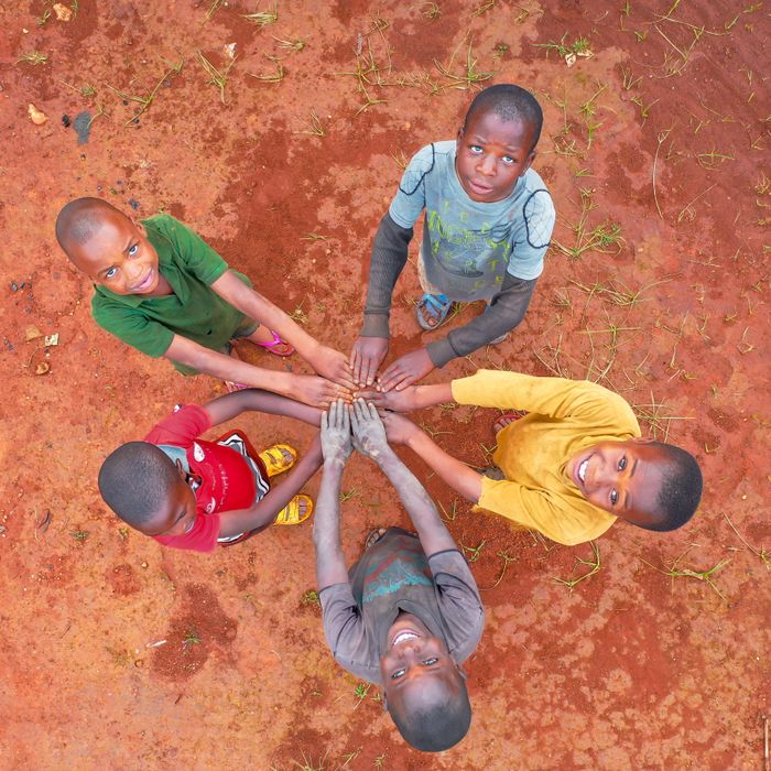 Top-down shot of five children holding hands on red earth in Makete, Tanzania.